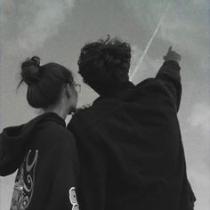 two people standing next to each other flying kites on a cloudy day in black and white