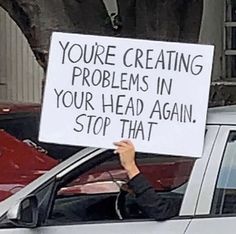 a woman holding up a sign that says you're creating problems in your head again, stop that