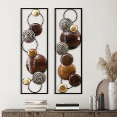 two metal wall art pieces sitting on top of a wooden dresser next to a vase