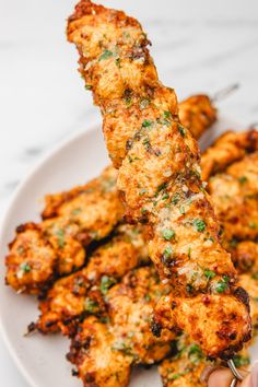 someone is cutting up some chicken skewers on a white plate with parsley