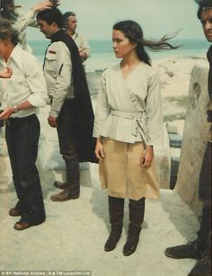 a group of people standing around each other near the ocean with one woman holding her hair