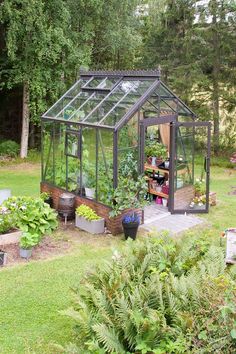 a small greenhouse in the middle of a yard with lots of plants growing inside it