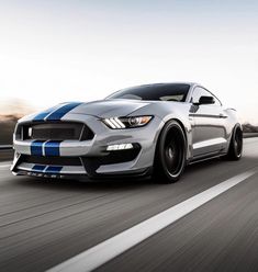 a silver mustang with blue stripes driving down the road