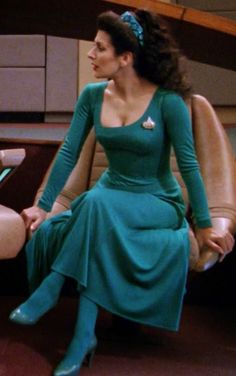 a woman in a green dress is sitting on a chair and looking off to the side