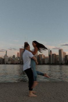 a man carrying a woman on his back near the water in front of a city skyline