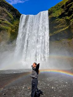 a woman standing in front of a waterfall with a rainbow