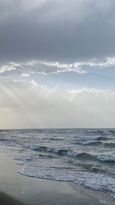 the sun shines through the clouds over the water at the beach on a cloudy day