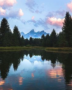 the mountains are reflected in the still water of this lake at sunset with clouds and trees