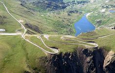 an aerial view of a winding road in the mountains with blue water on each side