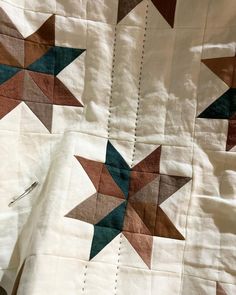 a close up of a quilt on a bed with white sheets and brown and blue stars