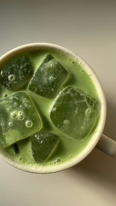 a cup filled with green liquid and ice cubes on top of it's side