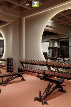 there are many gym equipment in this large room with mirrors on the wall and lights hanging from the ceiling