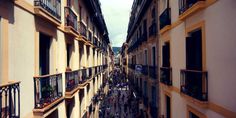 people are walking down an alley way between two buildings with balconies on each side