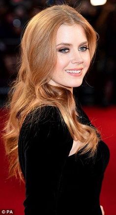 a woman with long red hair is smiling at the camera and wearing a black dress