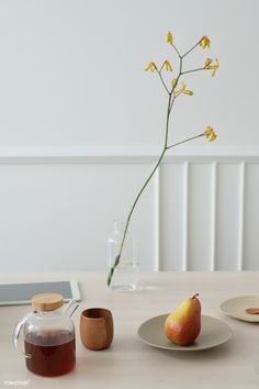 the table is set with two pears, a glass pitcher and a vase filled with flowers