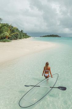 a woman sitting on top of a surfboard in the ocean next to a sandy beach