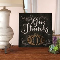 a sign that says give thanks on it next to a lamp and potted plant