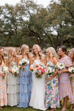 a group of women standing next to each other holding bouquets in their hands and smiling