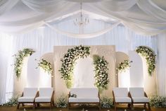 a wedding ceremony setup with white chairs and flowers on the back wall, draped in draping