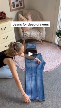 a woman in black shirt and jeans on floor next to dresser with blue jean's for deep drawers