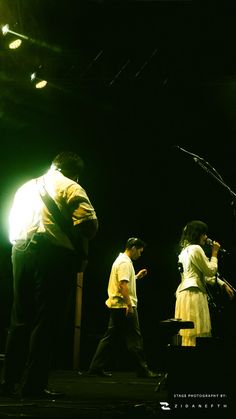 three people are performing on stage in front of microphones