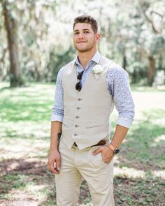 a man standing in the grass wearing a vest and tie with his hands on his hips