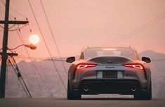 the rear end of a silver sports car driving down a road with power lines in the background