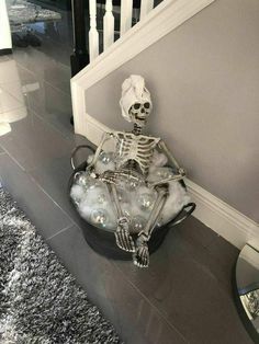 a skeleton sitting in a bucket filled with bubbles on the floor next to a stair case