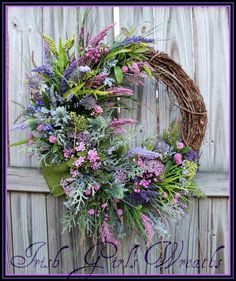 a wreath with purple flowers and greenery hanging on a wooden fence next to a door