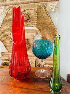 three different colored vases sitting on top of a wooden table next to each other