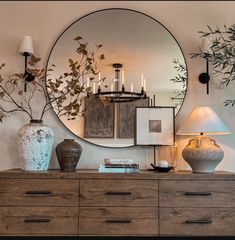 a dresser with vases and lamps on top of it next to a large round mirror