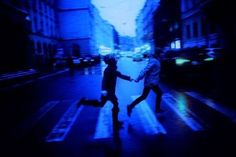 two people crossing the street at night with their hands in each other's pockets