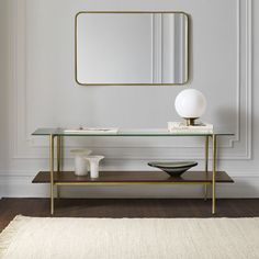 a table with a mirror, vase and lamp on it in front of a white wall