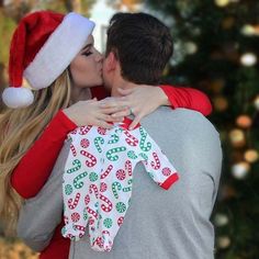 a man and woman kissing each other in front of a christmas tree with presents on it