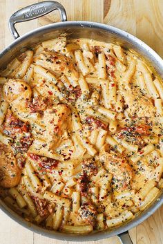 a pan filled with pasta and chicken on top of a wooden table