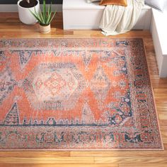 an orange and blue area rug on a wooden floor next to a potted plant