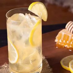 a glass filled with ice and lemons on top of a wooden table next to honey