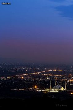 the city lights shine brightly at night from atop a hill in the distance, with an airplane flying overhead