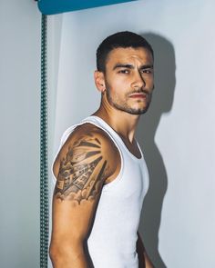 a man with a tattoo on his arm standing in front of a shower stall and looking at the camera