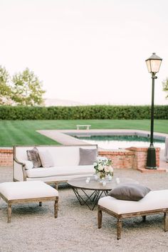 a white couch and chair sitting in front of a pool with a lamp post next to it