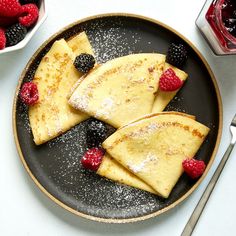 pancakes with raspberries and powdered sugar on a black plate next to silverware