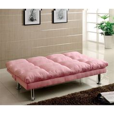 a pink futon sofa sitting on top of a white floor next to a plant