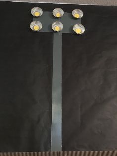 four lights on a metal pole in front of a black background with a ruler underneath it