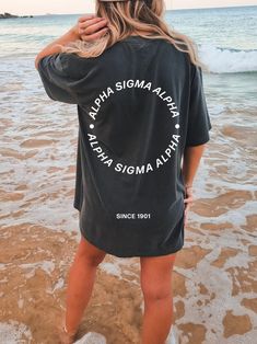 a woman standing on the beach in front of the ocean wearing a delta delta t - shirt