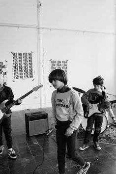 three young boys are playing guitars in a room with posters on the wall behind them