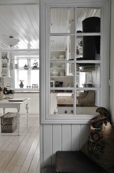 a room with white walls and wood flooring has a window to the kitchen area