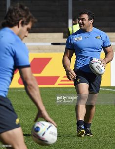 two men in blue shirts are playing rugby on the field with one holding a ball