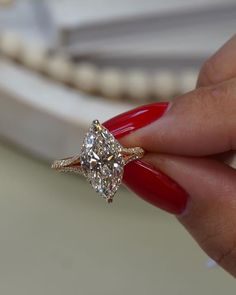 a woman's hand holding a diamond ring with red nails on her fingers,