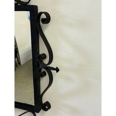 a mirror hanging on the side of a white wall next to a black wrought iron frame