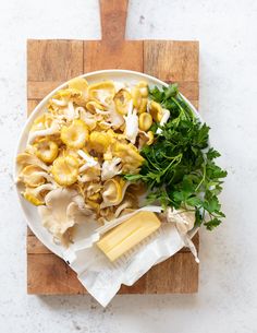 a white plate topped with pasta and greens next to a cheese wedge on top of a cutting board